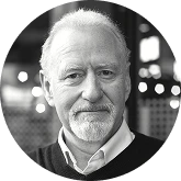 Grayscale portrait of an older man with short white hair and a light beard, wearing a collared shirt.