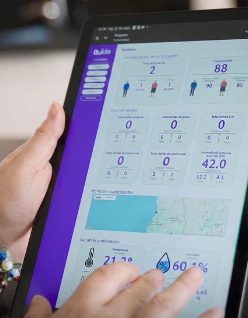 Tablet held in a left hand shows a purple dashboard with charts and stats about participant characteristics on the screen.