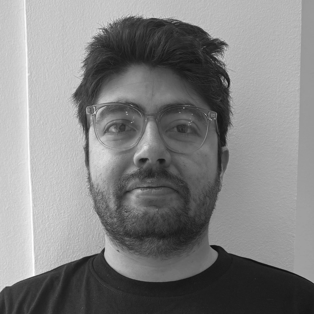 Black-and-white head-and-shoulders portrait of a man with glasses and a beard standing against a light wall.