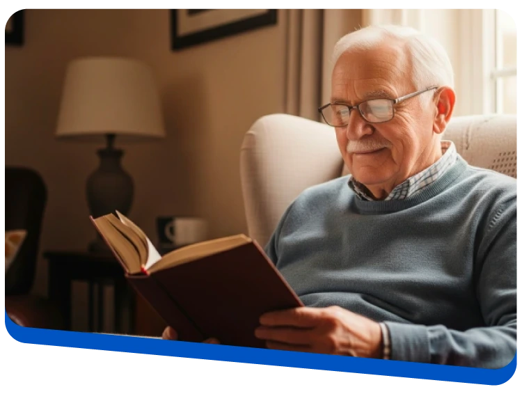 Elderly man with glasses reading a book while seated in a cozy living room.